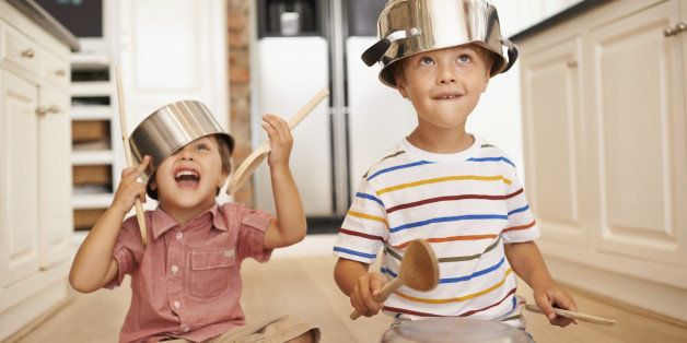 Two young boys sitting on the kitchen floor playing with pots and pans