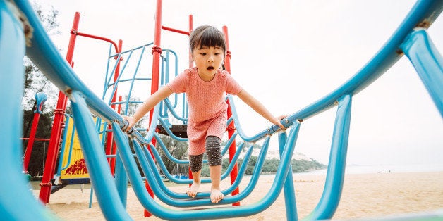 Lovely little girl playing joyfully with the climbing equipments in sand playground.