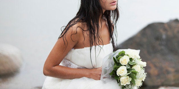 Sad bride sitting on the sea-shore and crying in the rain