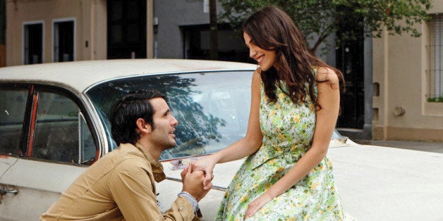 Young man proposing to woman against car, smiling