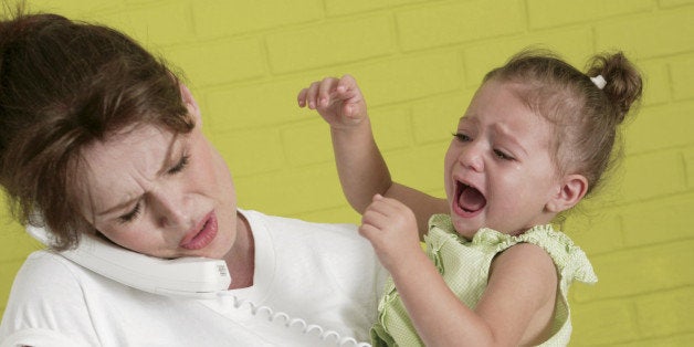 Pregnant woman holding crying girl while talking on telephone