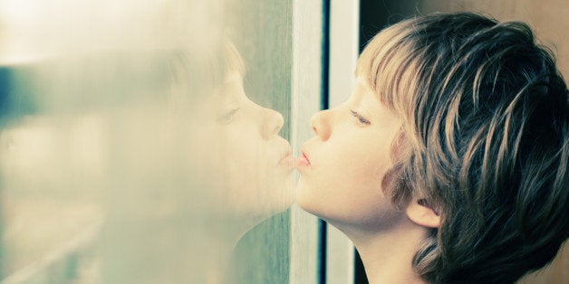 Cute 6 years old boy looking through the window