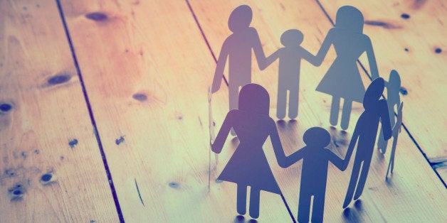 A family paper chain ring on a wooden background. The chain is made up of adult and child male and female characters.