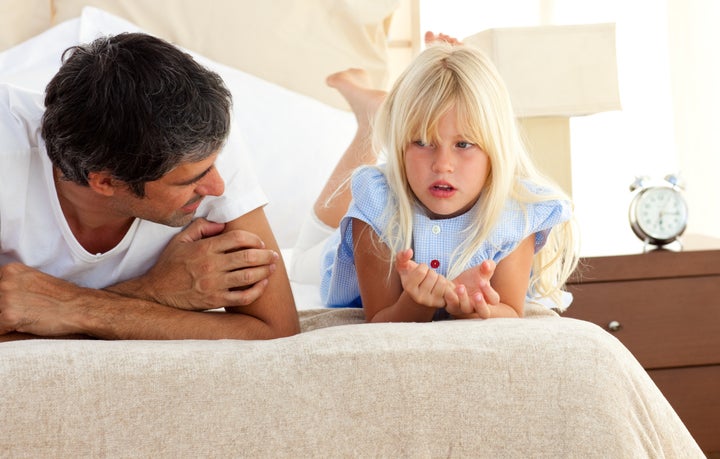 Little girl talking seriously with her father lying on bed