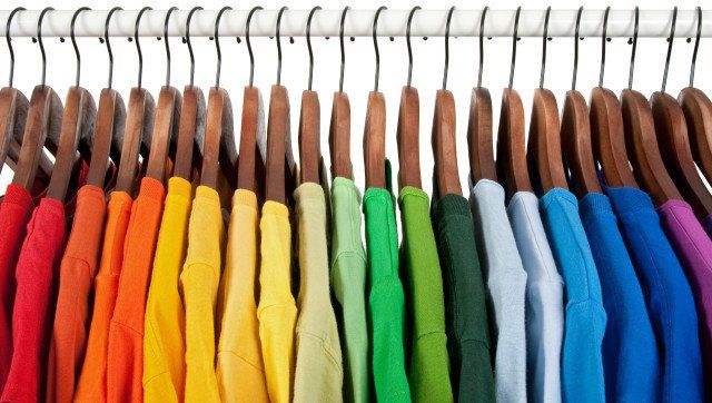 Rainbow colors. Choice of casual clothes on wooden hangers, isolated on white.