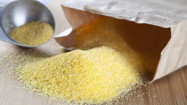 Bag of polenta spilling onto a cutting board with tablespoon in the background