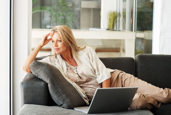 Portrait of a thoughtful middle aged woman lying on sofa while using laptop
