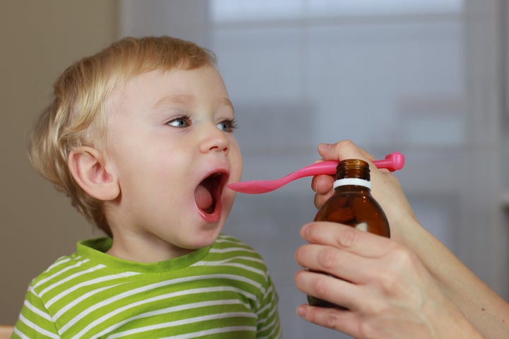 Mother giving 2 years old baby boy medicine, cough syrup on a spoon. Sick child.