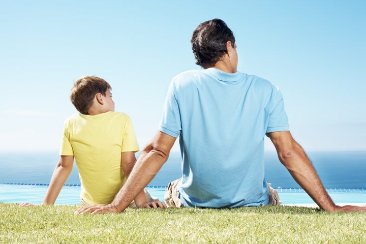 Father and little son sitting on grass and looking at scene - Rear view