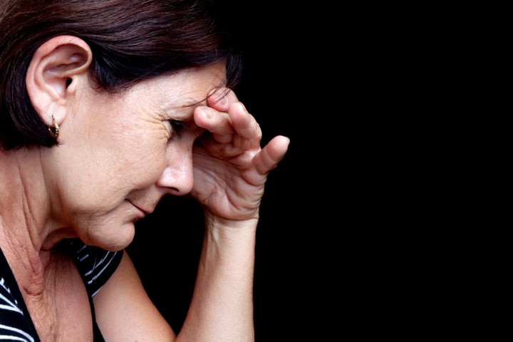 Portrait of a depressed older woman suffering from stress or a strong headache isolated on black