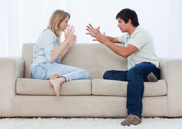 A young couple sitting on a couch are having an argument