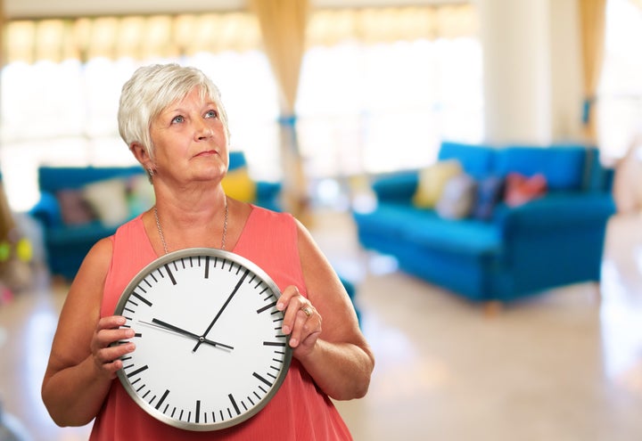 senior woman holding a clock ...