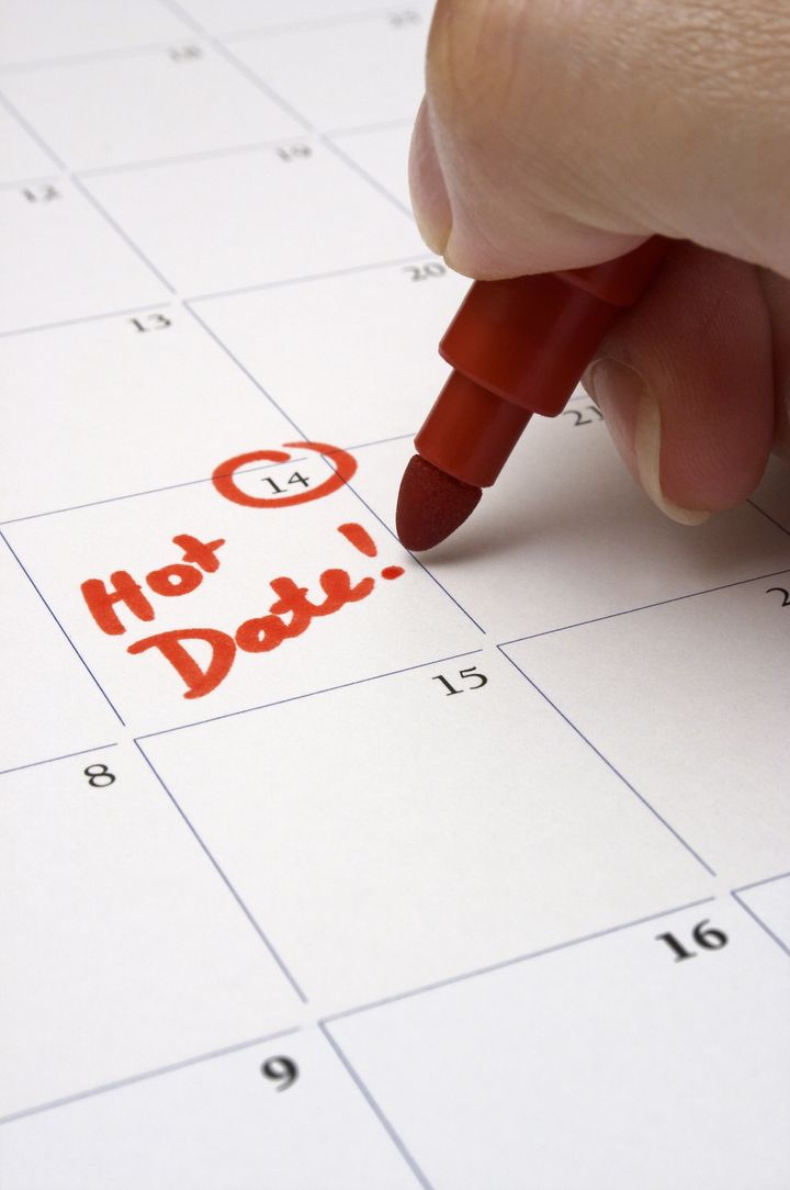 A person writing down the appointment for a date on the calendar. Shallow depth-of field - focused on the words "Hot Date".