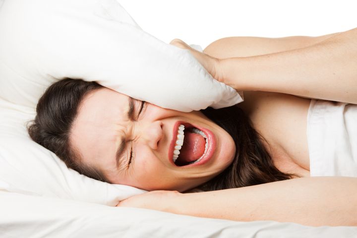 A frustrated tired woman hides her head in her pillow and screams because she can't sleep. Isolated on white.