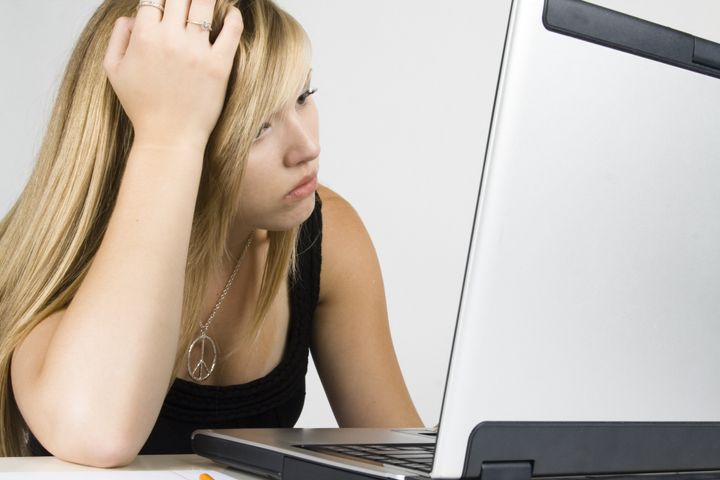 Young woman sitting in front of a computer looking bored.