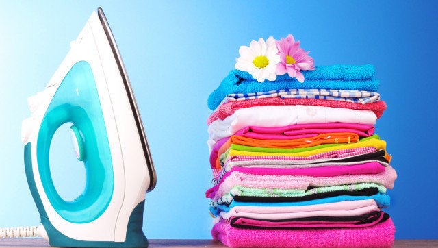 Pile of colorful clothes and electric iron on blue background