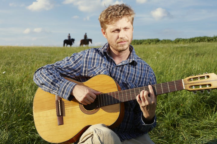 young blonde man strumming a...