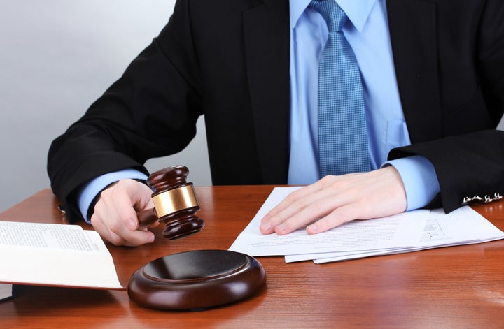 wooden gavel in hand and books on wooden table on gray background