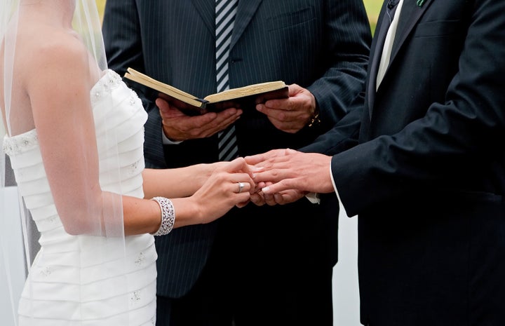 bride and groom holding hands during ring exchange part of an outdoor wedding ceremony