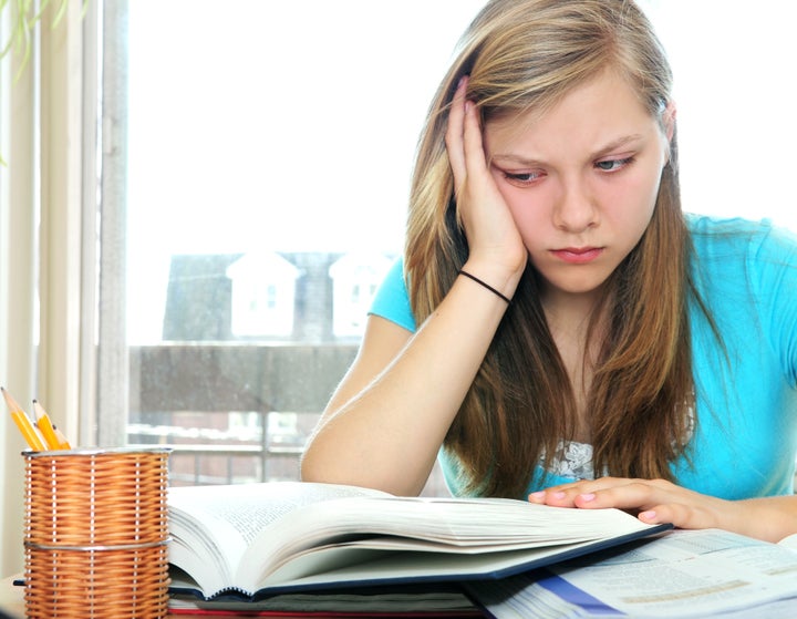 Teenage girl studying with textbooks looking unhappy