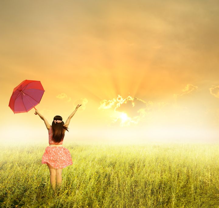 Beautiful woman holding red umbrella in grass field and sunset