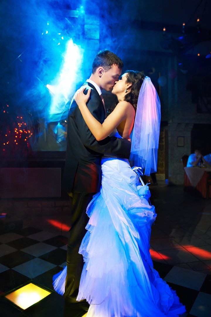 Kiss and dance young bride and groom in dark banqueting hall