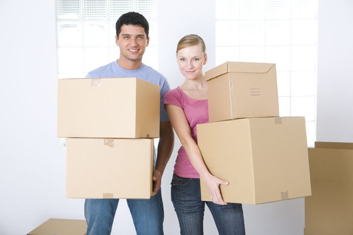 Young couple holding cardboard boxes. They're smiling and looking at camera. Front view.