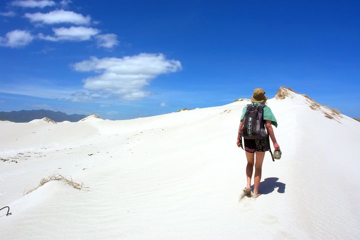 woman walks uphill dune under...