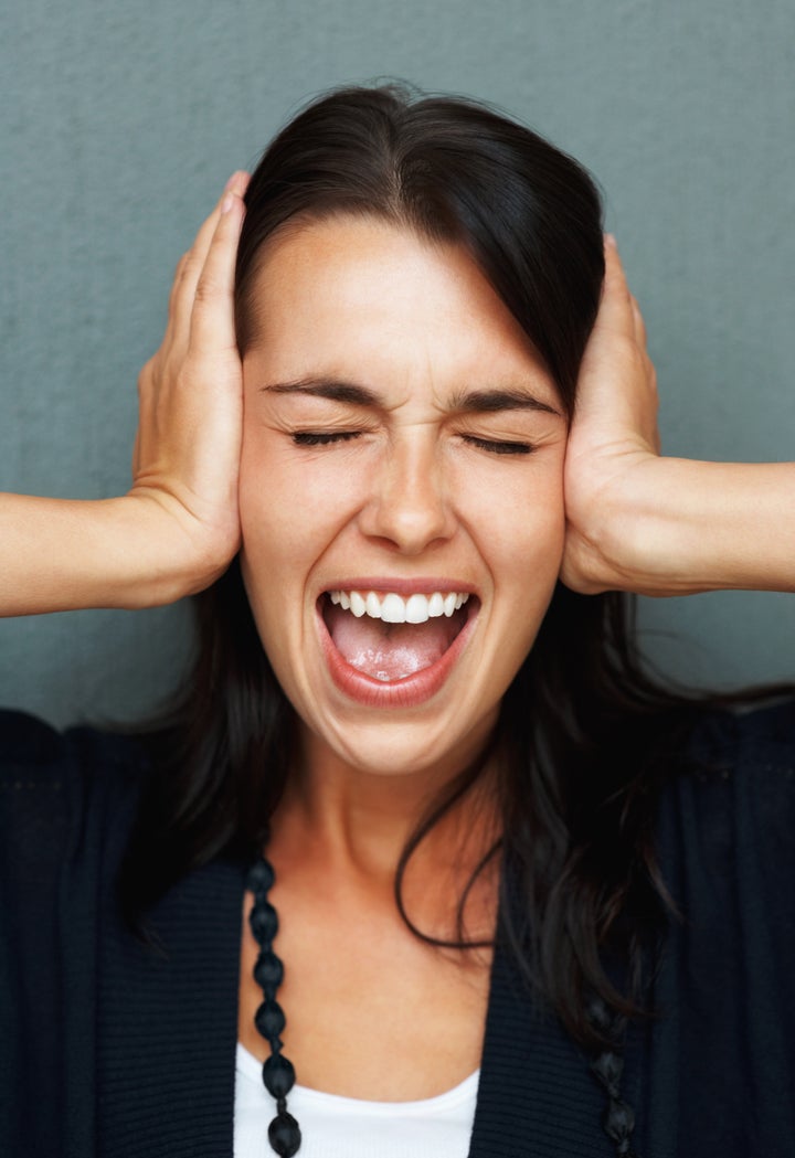 Woman screaming while covering her ears and shutting eyes in frustration