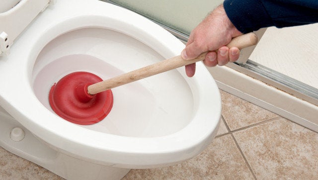 A plumber uses a plunger to unclog a toilet.