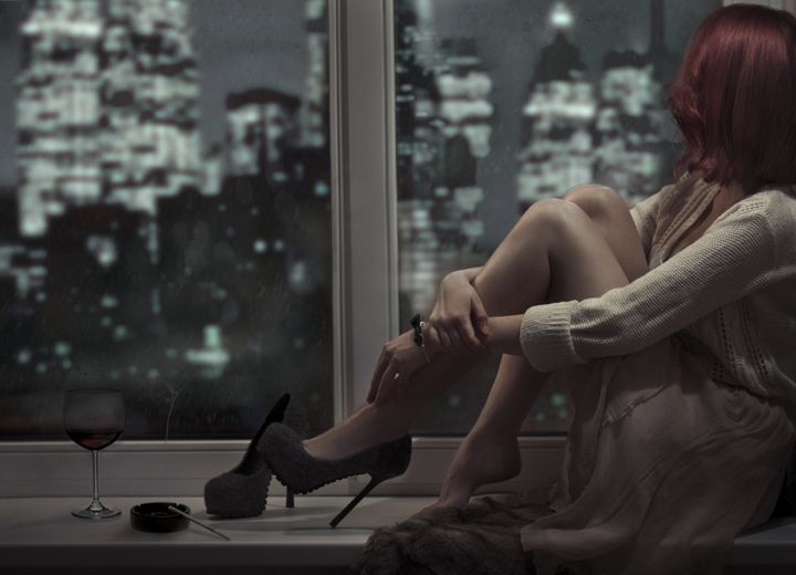 Alone beautiful woman sitting on window and looking on night city