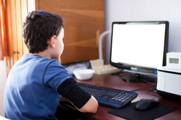 Selective focus indoor shot of a boy reading his computer's screen