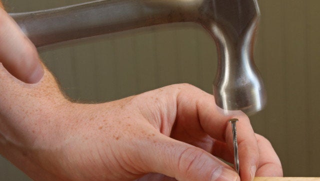 A person hammering a nail into a piece of wood.