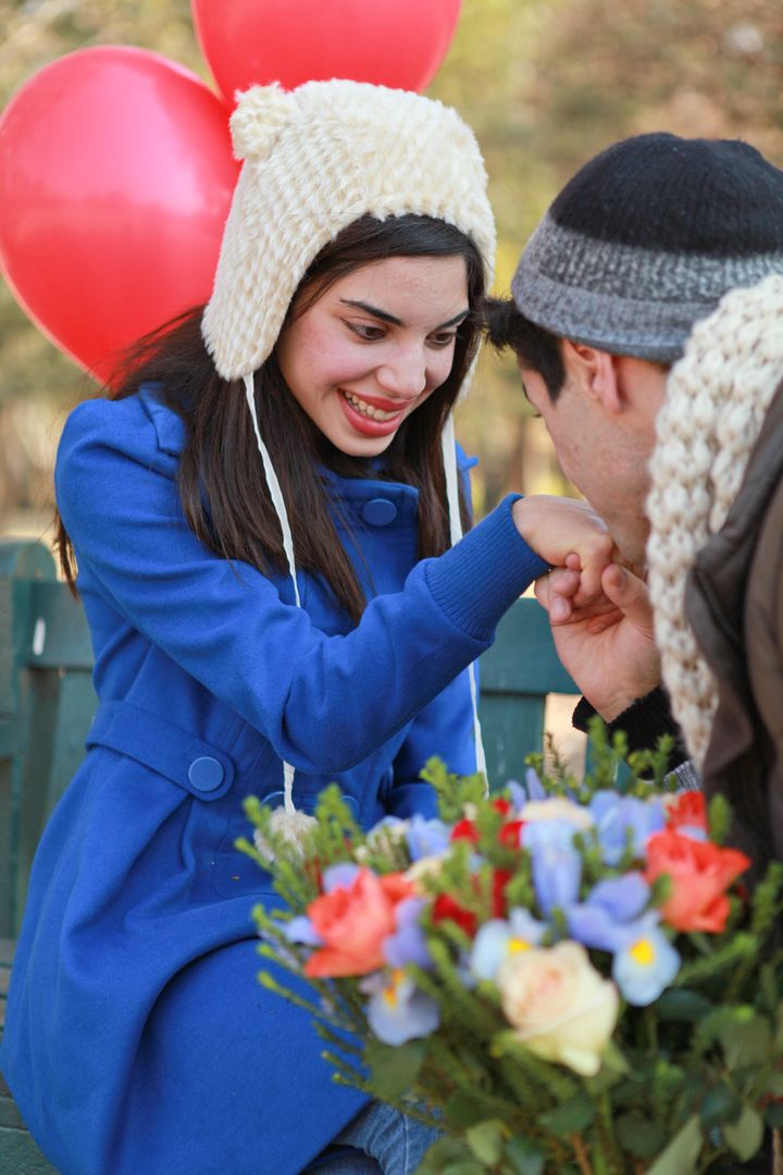 Young attractive caucasian couple in love sitting on a bench in the park in autumn or winter with balloons and flowers while the man proposes marriage to the woman