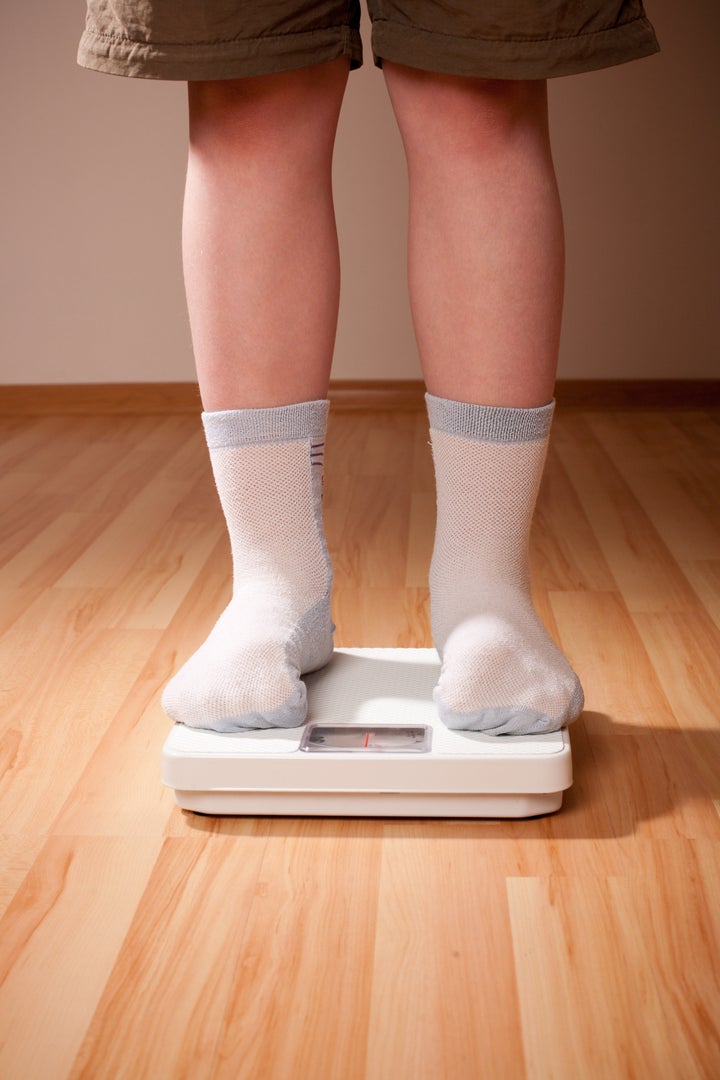 Boy measures weight on floor scales. Legs in shorts and socks standing at floor scales on hardwood floor in living room.