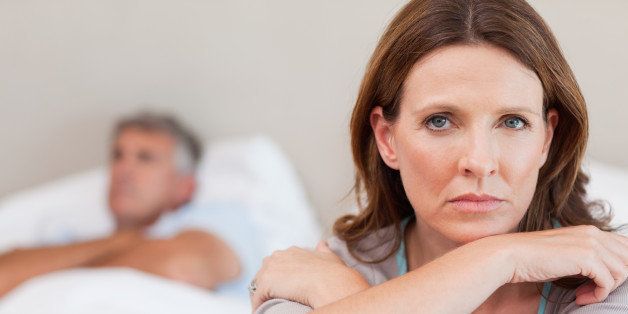 Sad woman on the bed with her husband in the background