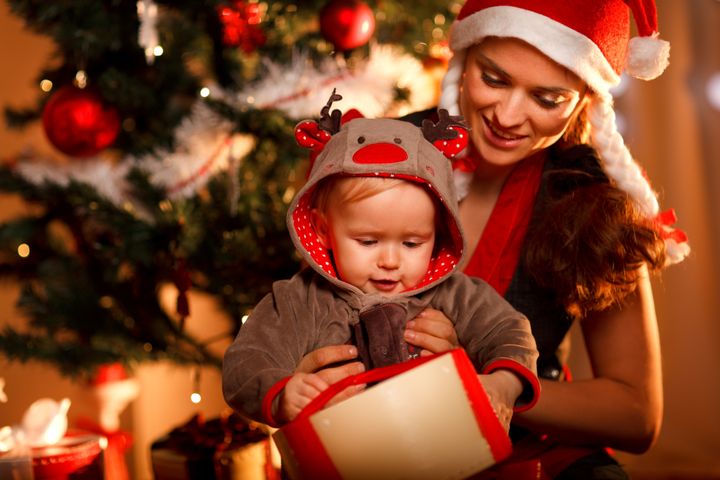 Young mother helping interested baby open present box at Christmas tree