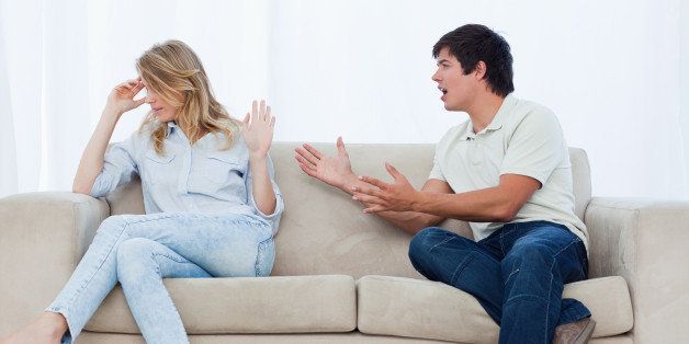 A man sitting on a couch is having an argument with his girlfriend who has her head turned away