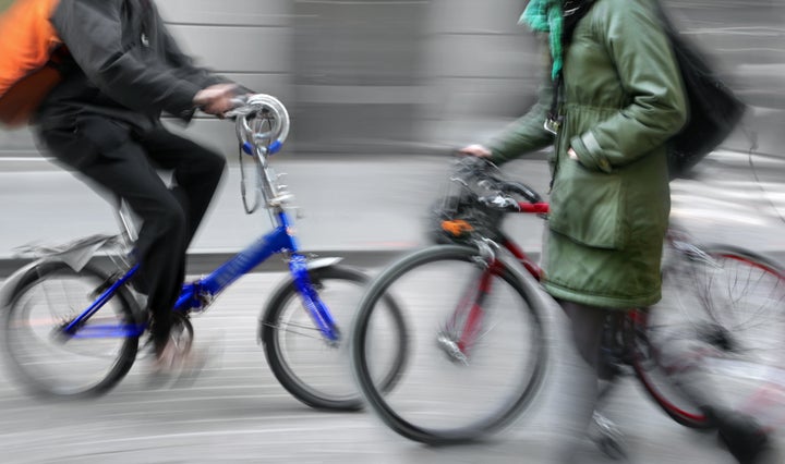 motion blur woman holding bicycle walking on the sidewalk, alternative urban transportation concept, bike rider in the background