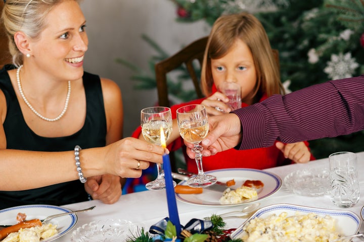 Family eating a traditional Christmas Dinner in front of the Christmas tree, the parents drinking wine clinking the glasses