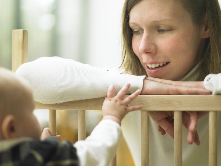 Mom Smiling at Baby Over Playpen Railing. Horizontally framed shot.