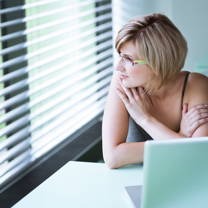 Portrait of a young woman pensively looking out of the window while sitting in front of her laptop