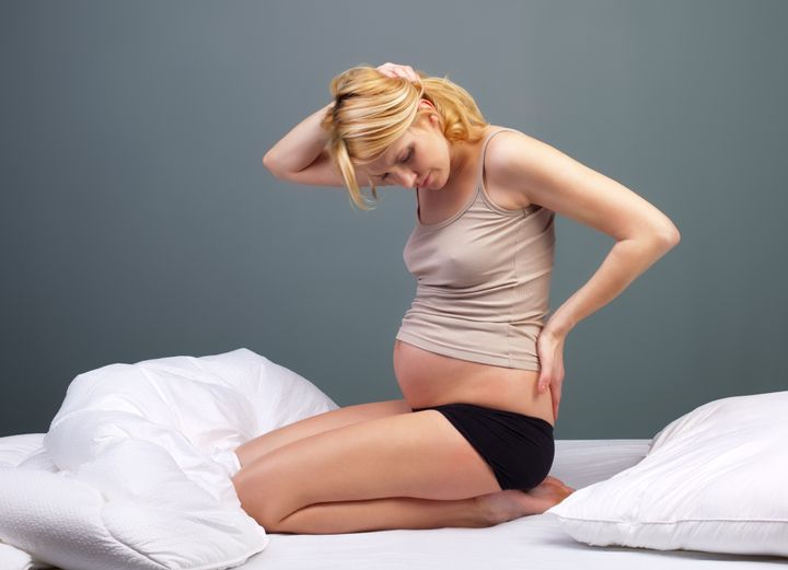 Young tired pregnant woman sitting on bed