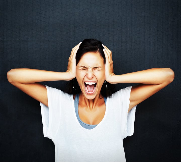 Woman holding head and screaming against blue background