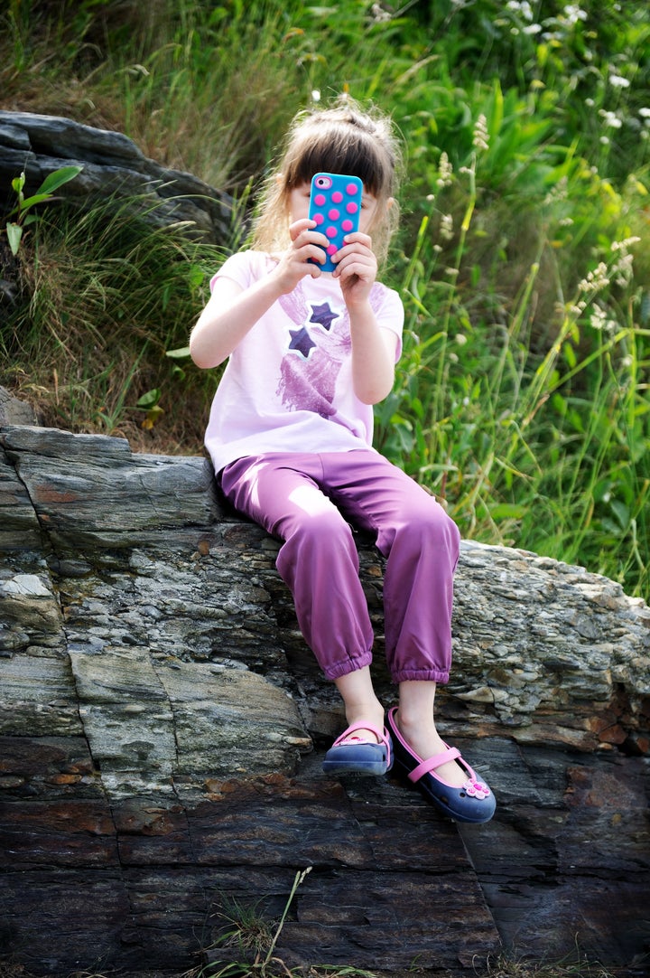 Little girl sitting on the rocks with mobile phone taking snapshots