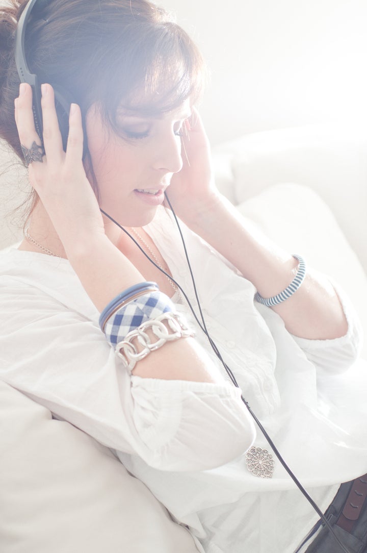 Happy woman with headphones lying down on sofa in lounge, listen to music