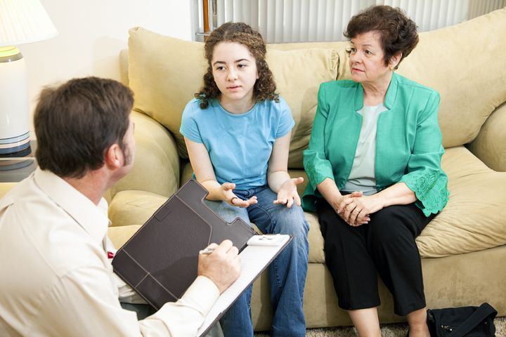 Worried mother looks on as her daughter talks to a therapist.