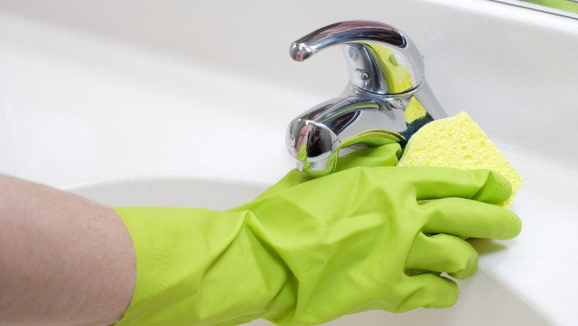 A person cleaning the bathroom sink with a glove