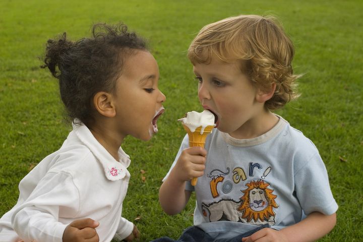Two young children sharing an ice cream, one a blonde boy the other a mixed race girl.