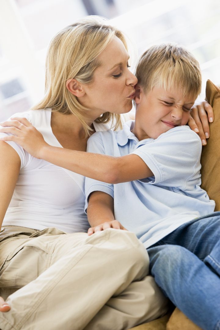 Woman kissing disgusted young boy in living room